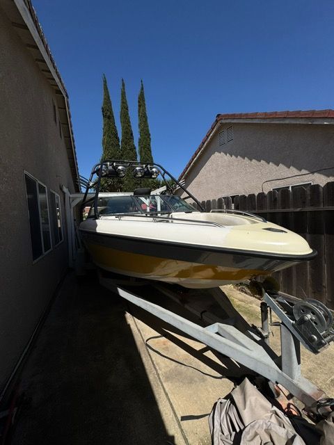 Speedboat stored in a narrow side yard between houses, with a trailer under a clear blue sky.