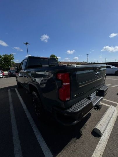 Black pickup truck parked in a sunny lot, rear view with trailer hitch and red taillights.
