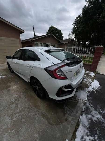White hatchback car parked in a wet driveway beside a house, with patches of snow nearby