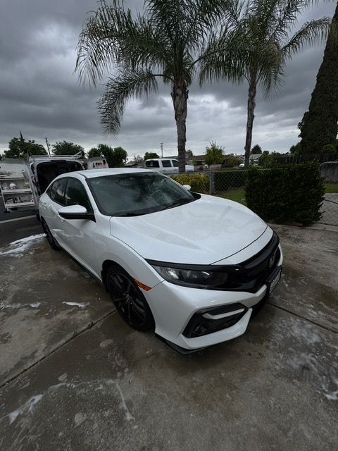 White Honda Civic parked on wet pavement under palm trees on a cloudy day