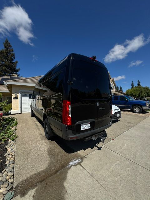 Black van parked in a driveway beside a house under a blue sky