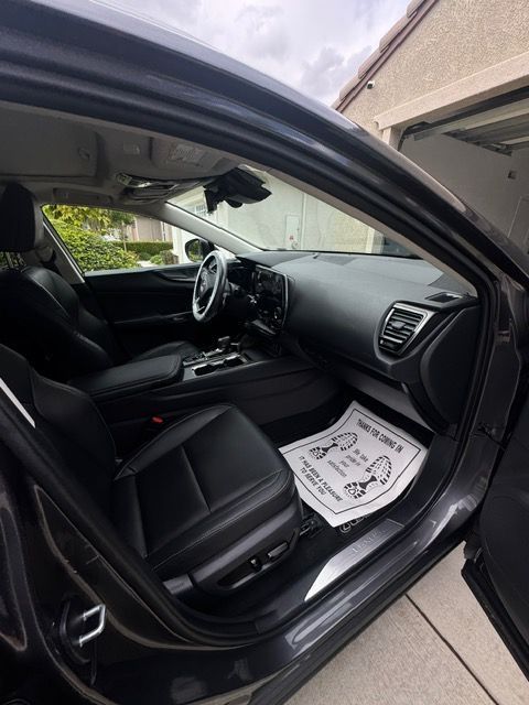 Open car door showing black front interior, steering wheel, and floor mats near a garage.