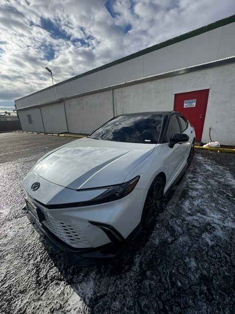 White car parked beside a gray warehouse wall near a red door on a snowy day