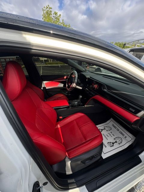 Red leather car interior with racing seats, steering wheel, and open door visible.