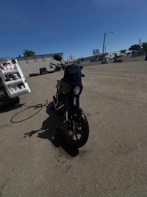 Black motorcycle parked on an open asphalt lot under a clear blue sky.