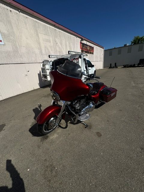Red touring motorcycle parked in a sunlit lot beside a white industrial building.