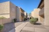 Exterior walkway between tan, stucco apartment buildings with desert landscaping under a clear blue sky.