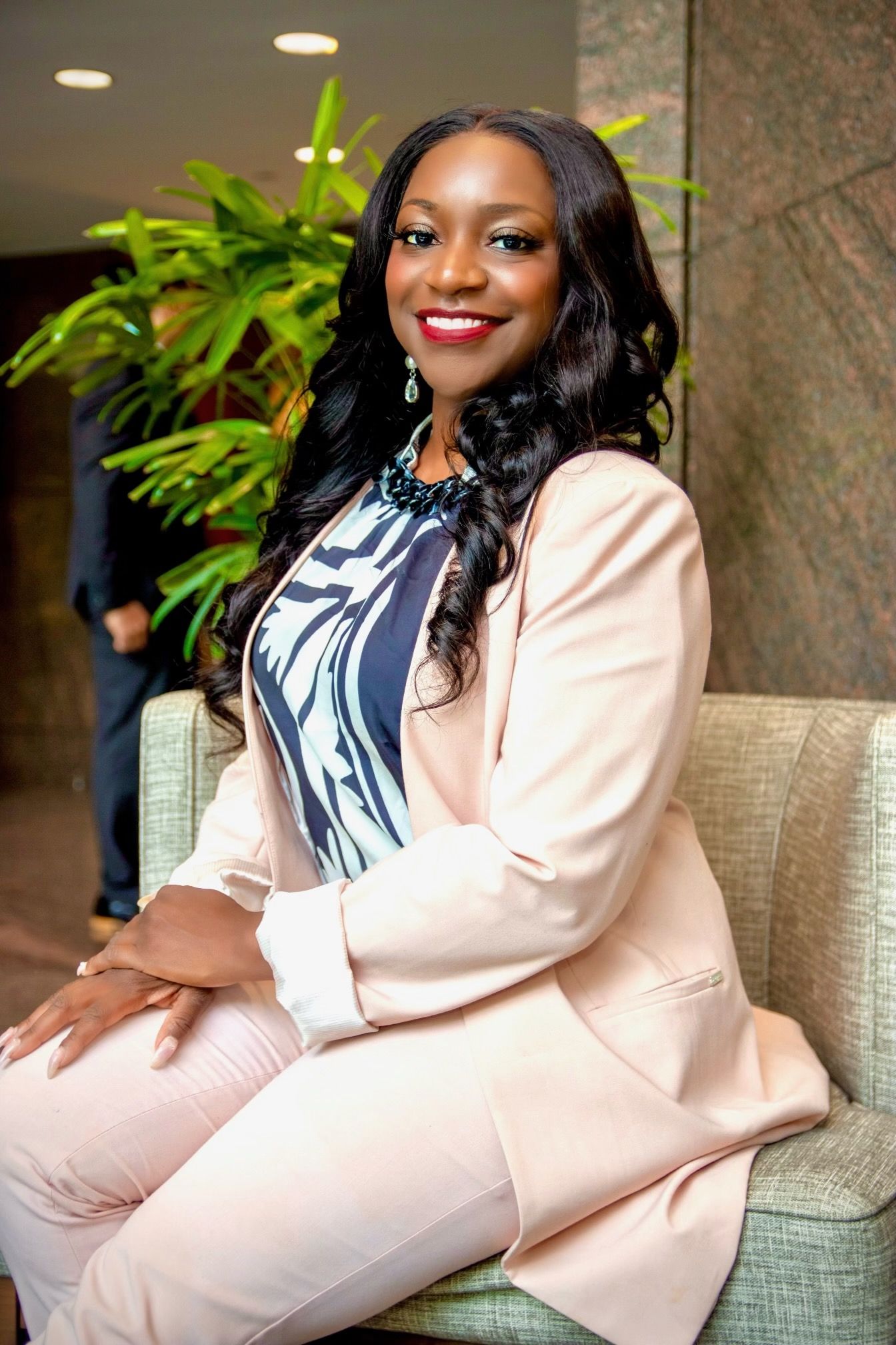 A woman in a suit is sitting in a chair and smiling.