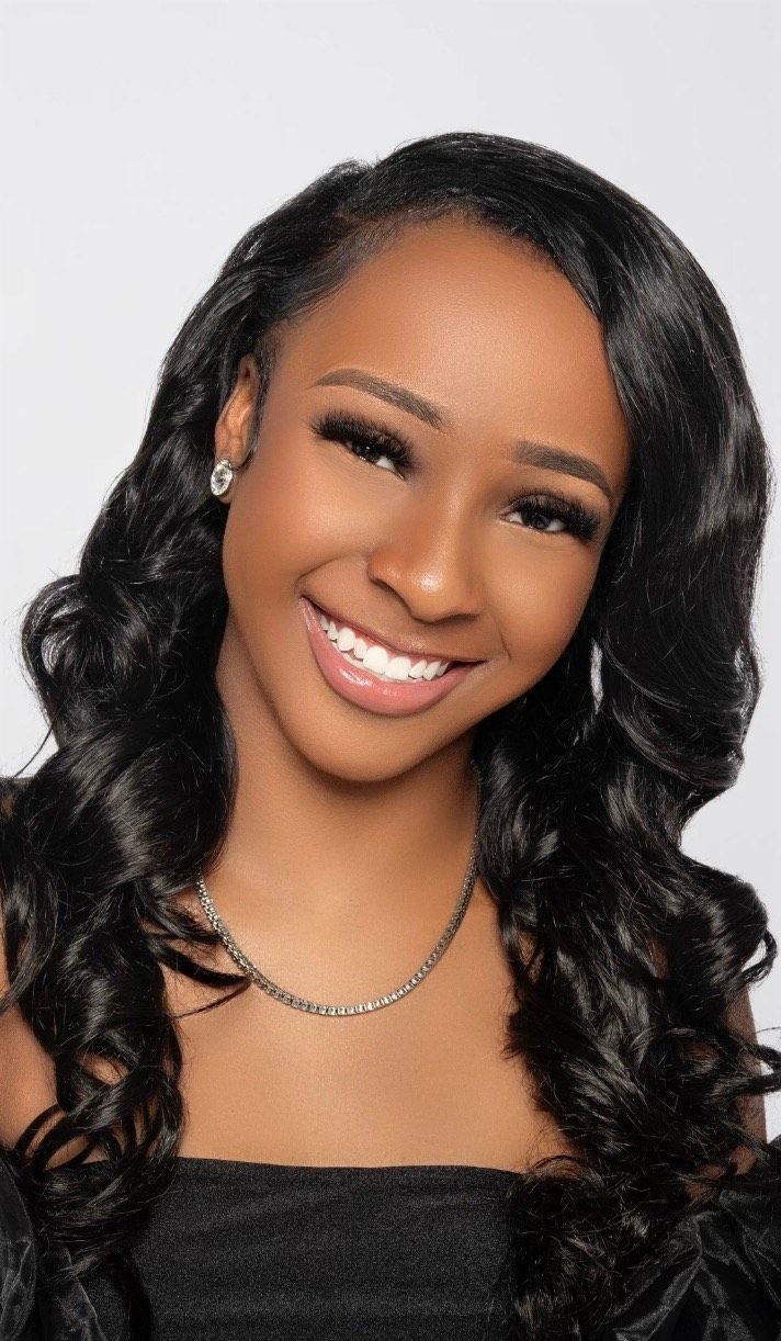 A woman with long black hair and a necklace is smiling for the camera.