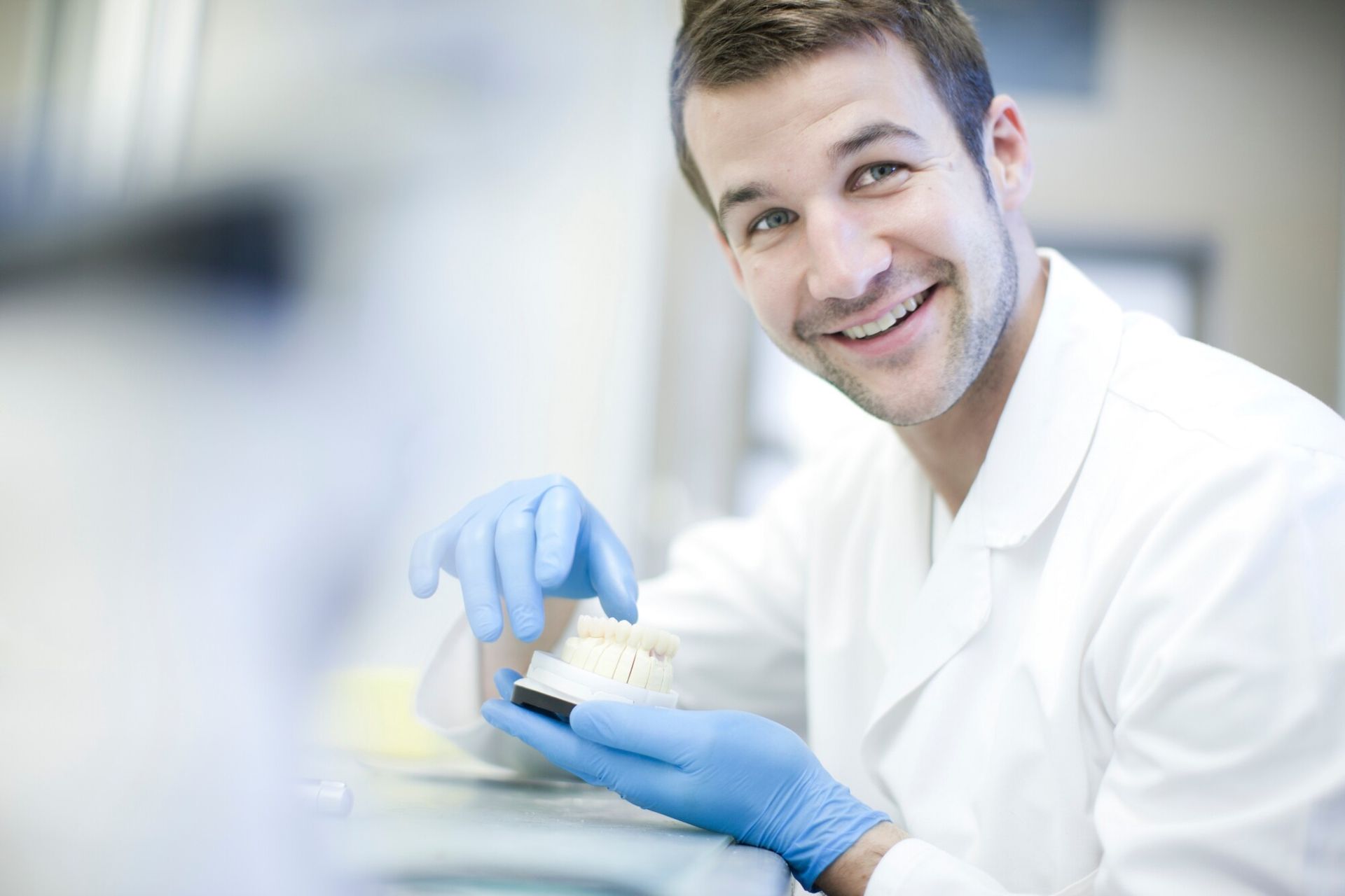 A man in a lab coat and blue gloves is holding a model of a tooth.