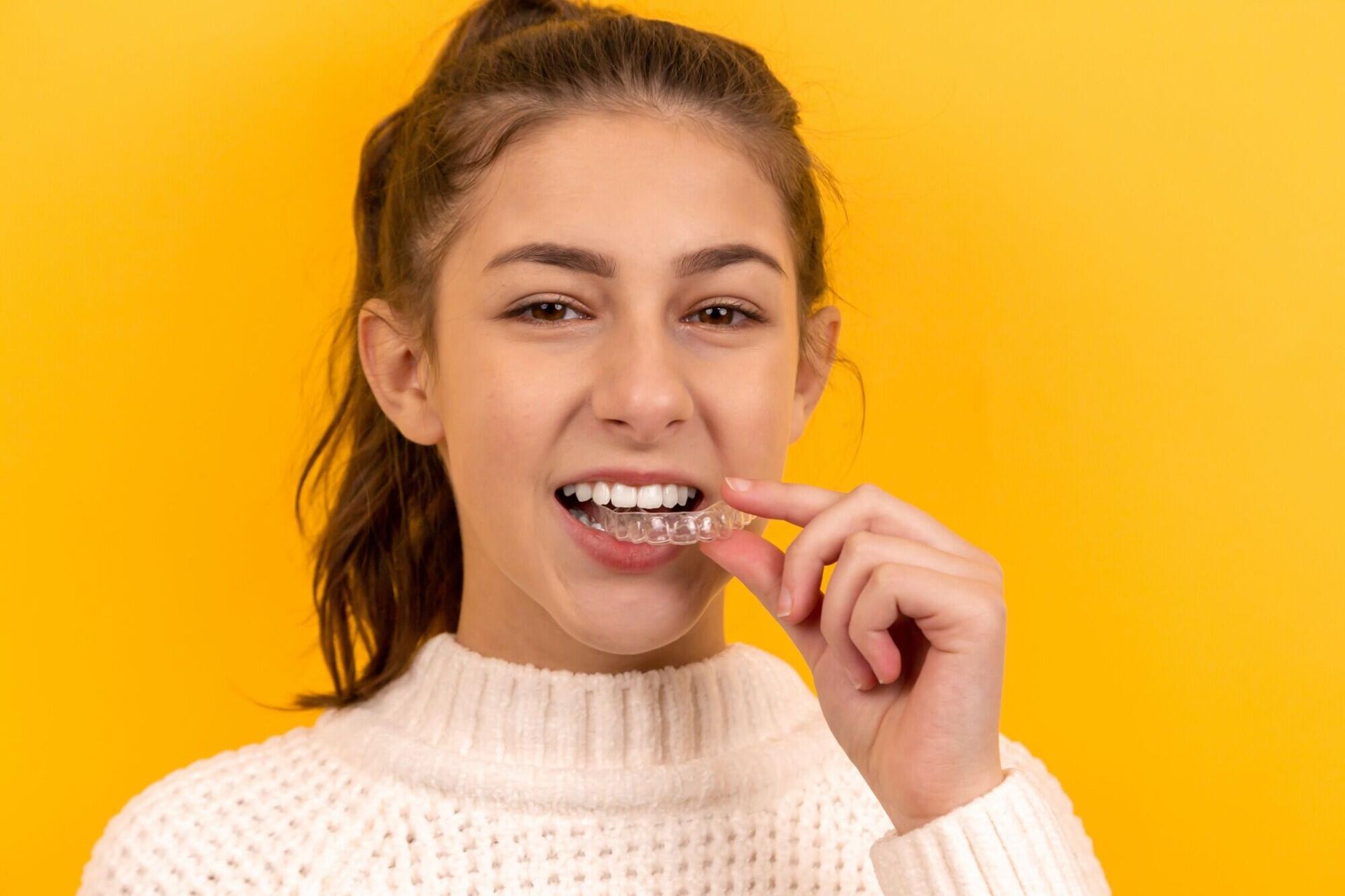 A young girl is holding a clear braces in her mouth.