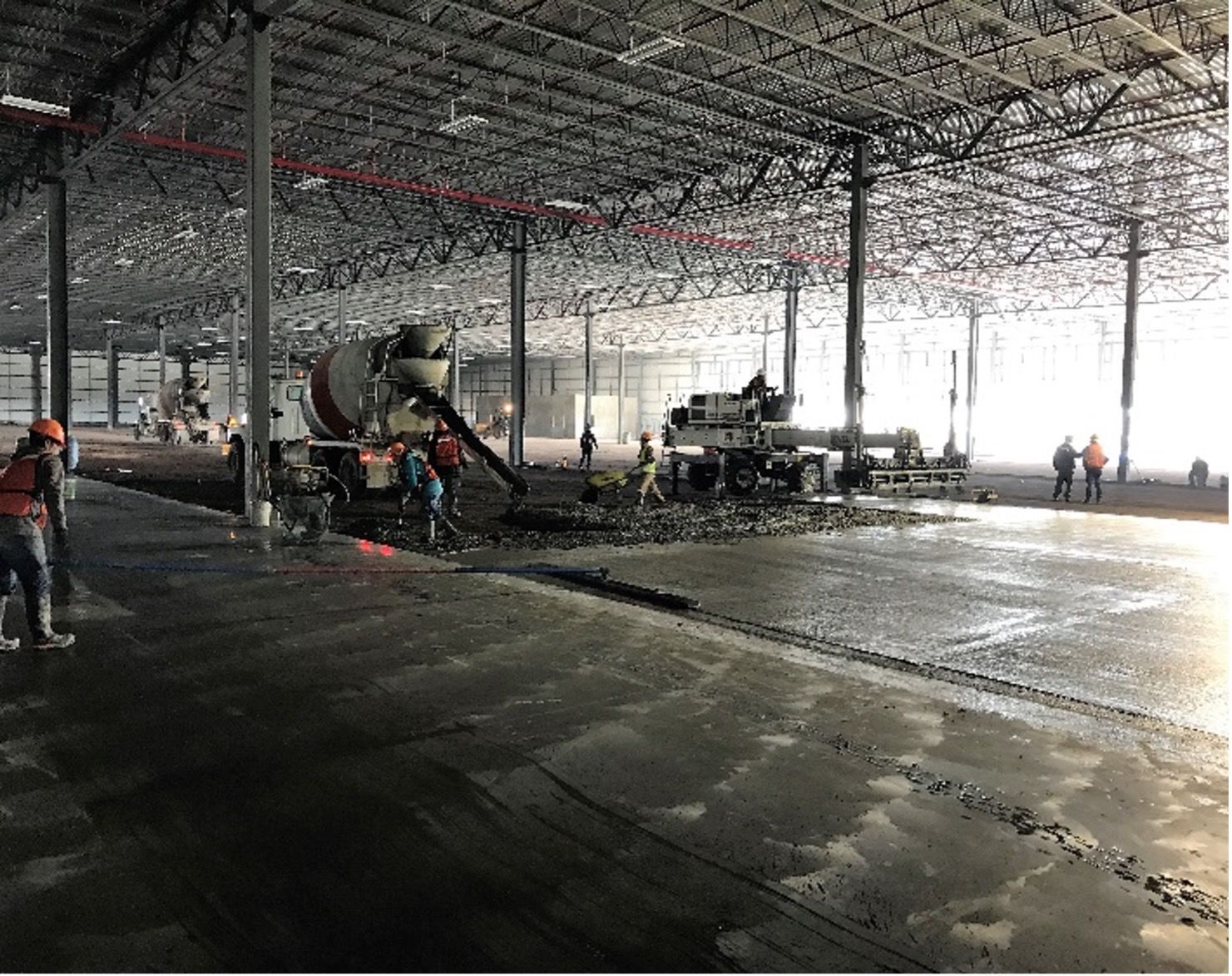 Vertido de hormigón en un gran almacén. Los trabajadores guían el flujo de hormigón desde un camión hasta el suelo.