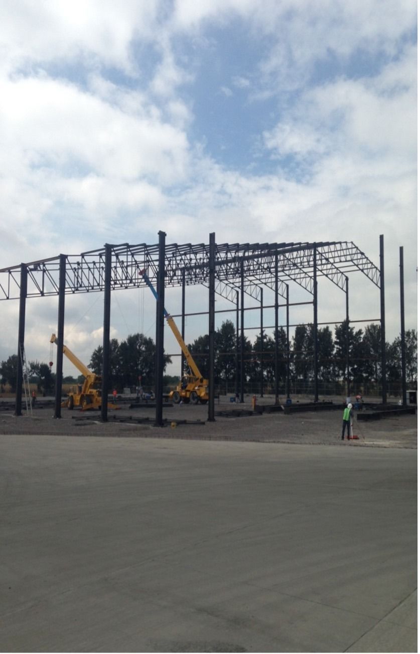 Estructura de acero de un edificio en construcción, con grúas y un obrero barriendo el suelo bajo un cielo nublado.