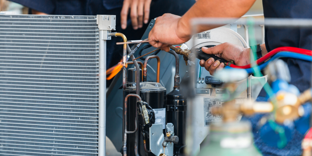 A man is working on an air conditioner with a wrench.