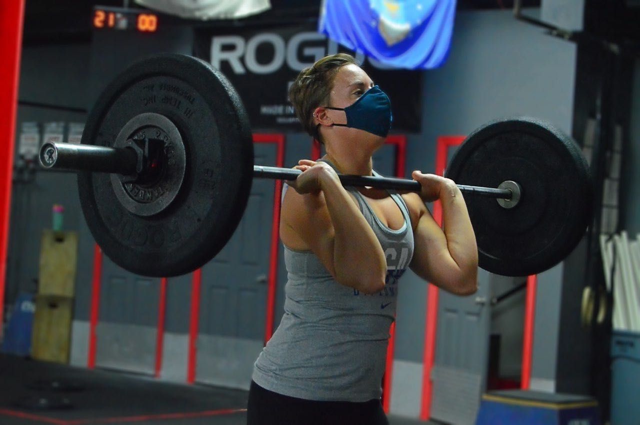 A woman wearing a mask is lifting a barbell in a gym
