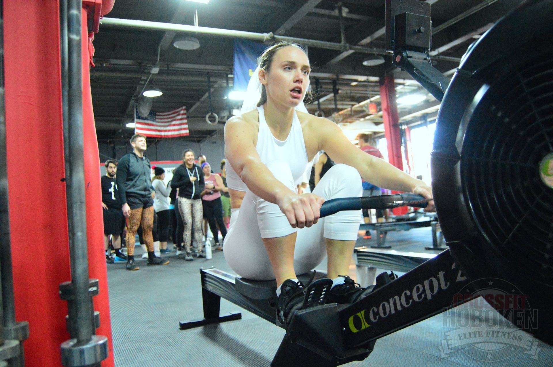 A woman is riding a concept 2 rowing machine in a gym.