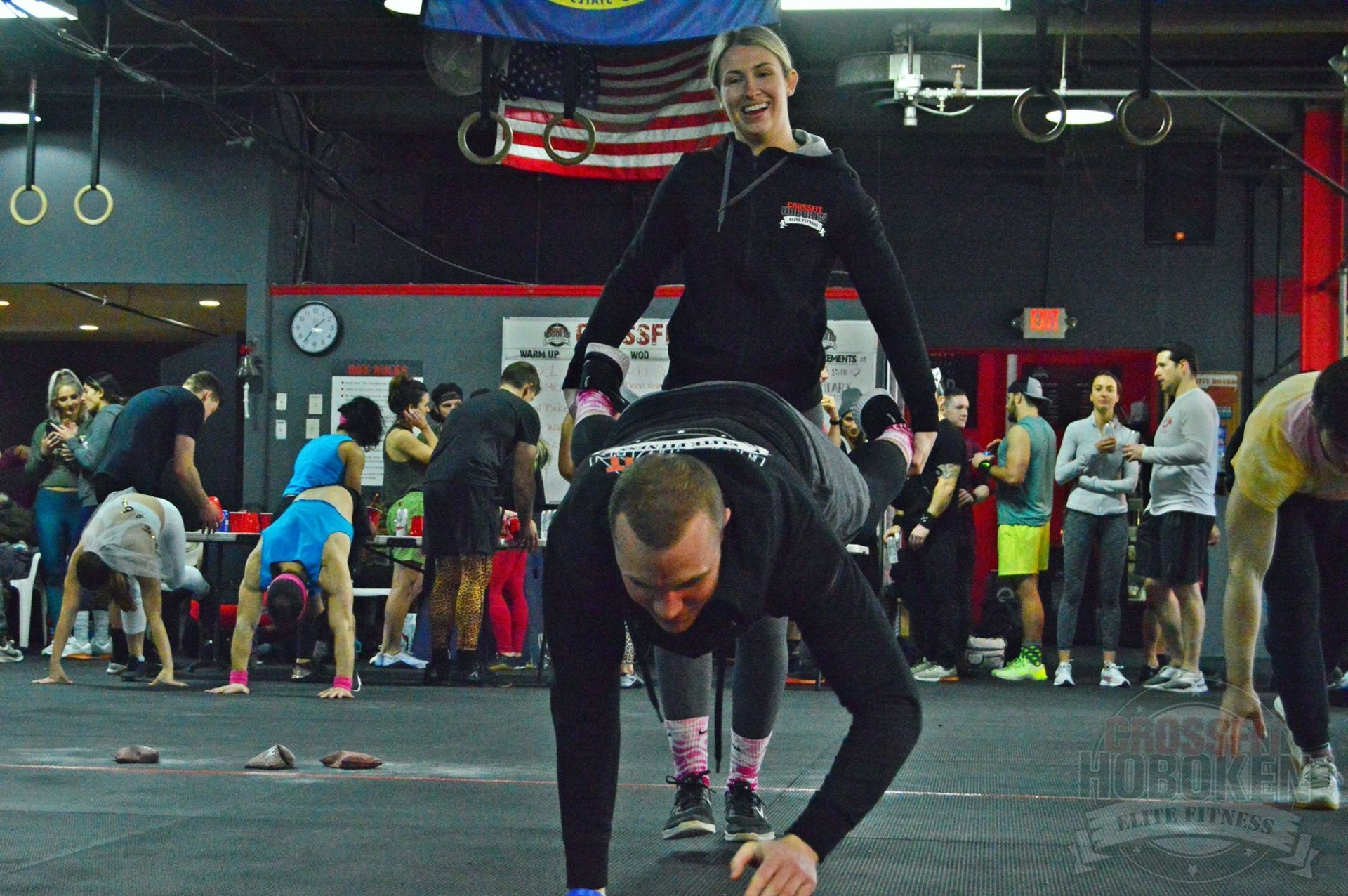 A woman is carrying a man on her back in a gym.