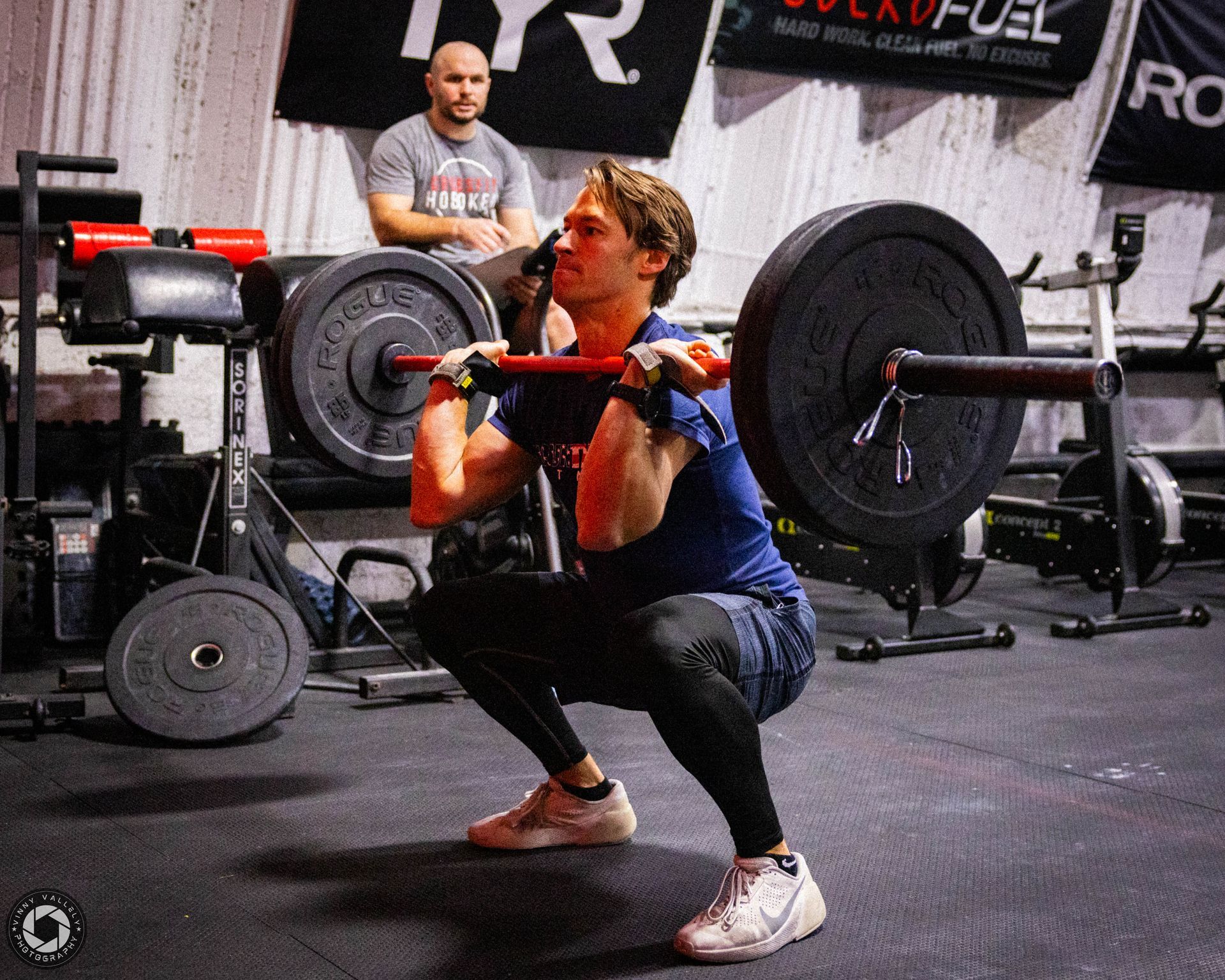 A man is squatting with a barbell in front of a sign that says crossfit hoboken.