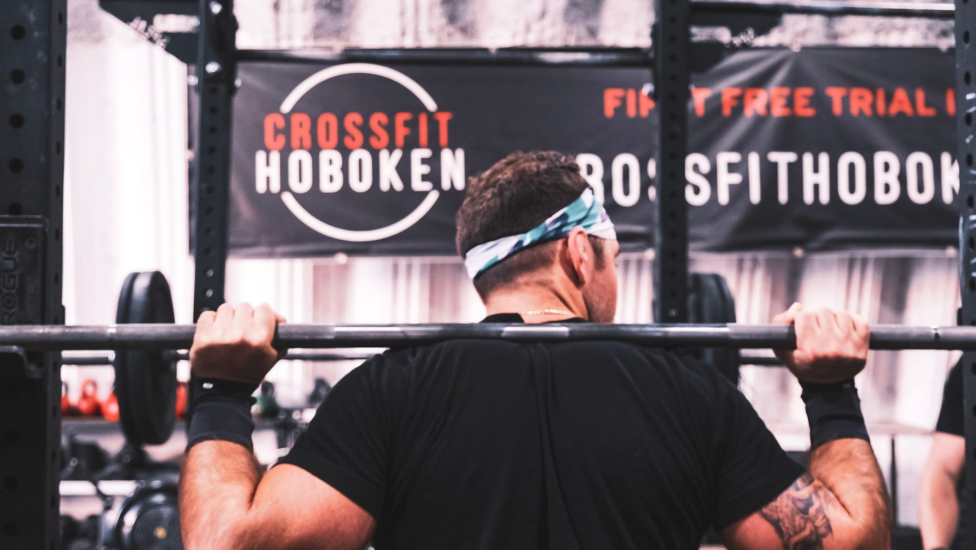 A man is squatting with a barbell in front of a sign that says crossfit hoboken.