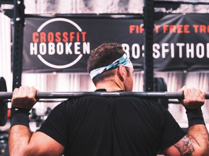 A man is squatting in front of a sign that says crossfit hoboken