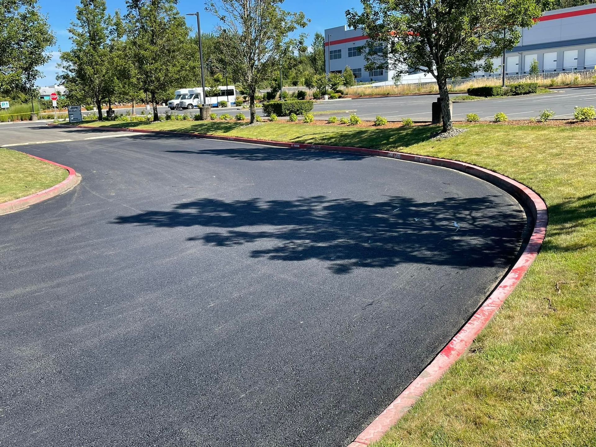 Asphalt driveway with red curb and grass, leading to a building on a sunny day.