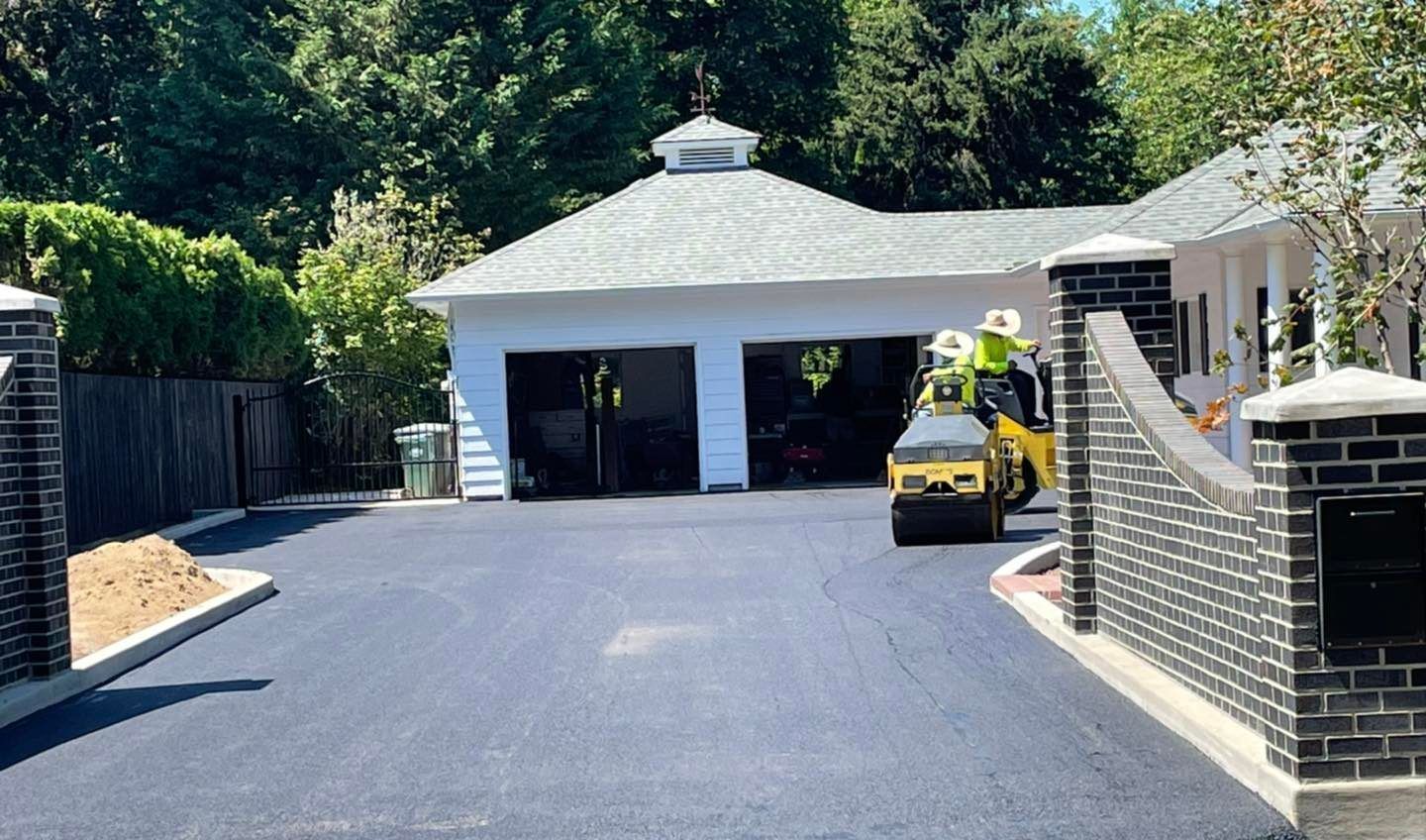 Paved asphalt driveway with a roller being used by workers in front of a white garage.