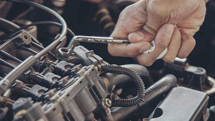 A hand using a wrench to work on a car engine.