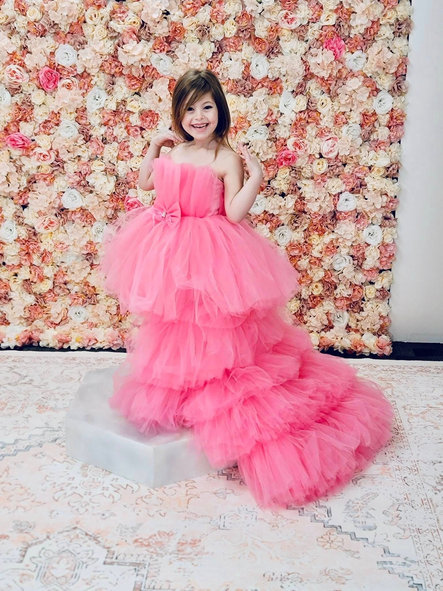 A little girl is wearing a pink tulle dress with a long train.