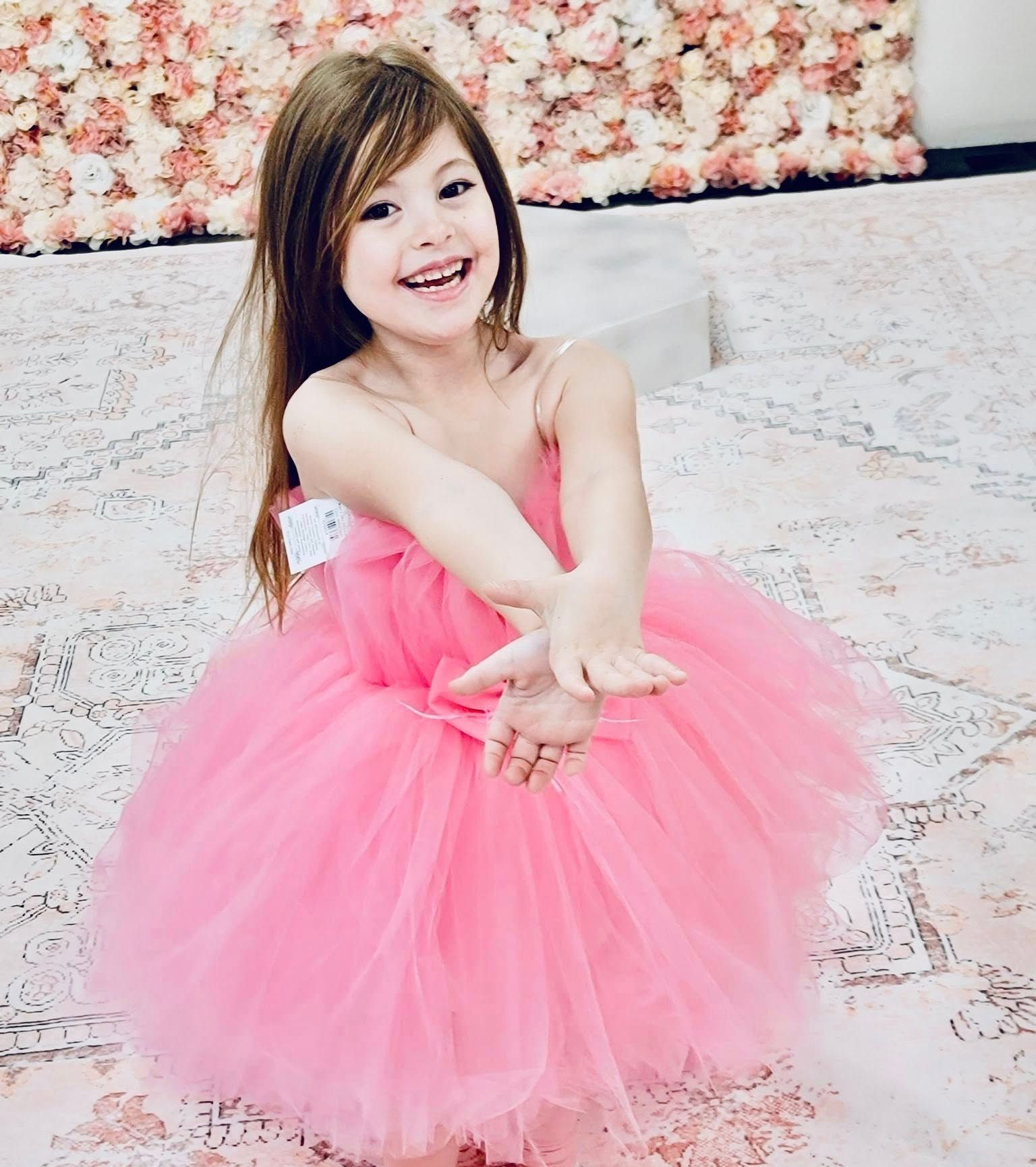 A little girl is wearing a pink tutu dress and smiling.