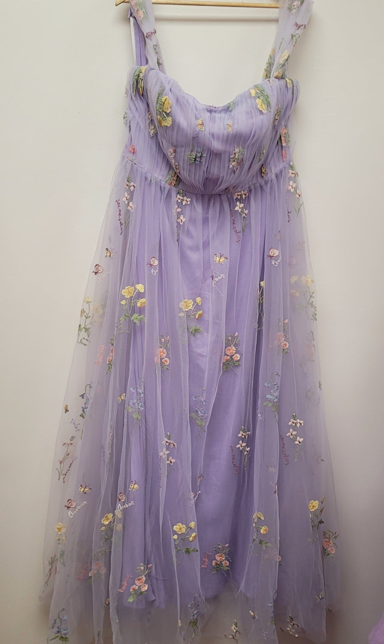 A purple dress with flowers on it is hanging on a hanger.