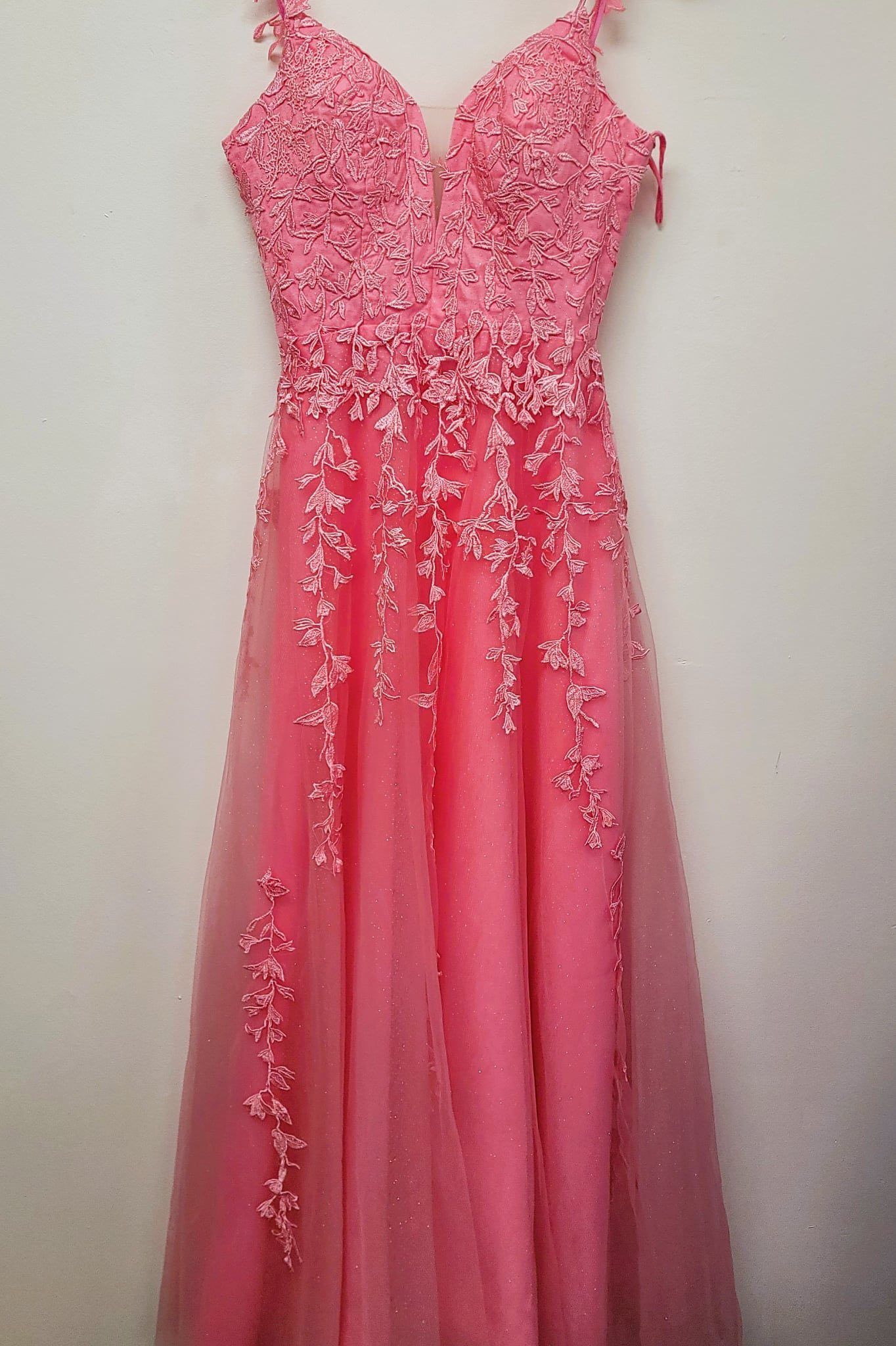 A pink dress is hanging on a white wall.