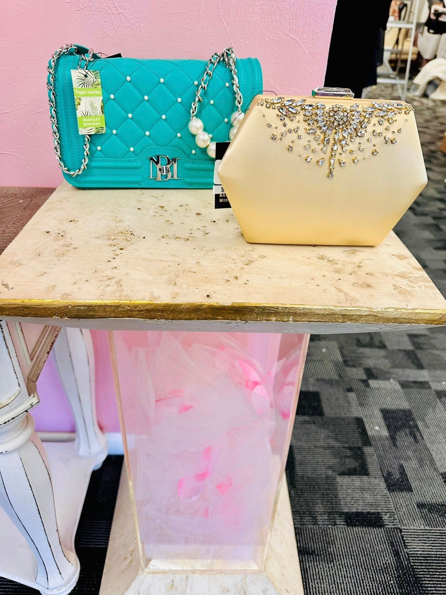 A blue purse and a gold clutch are on a table.
