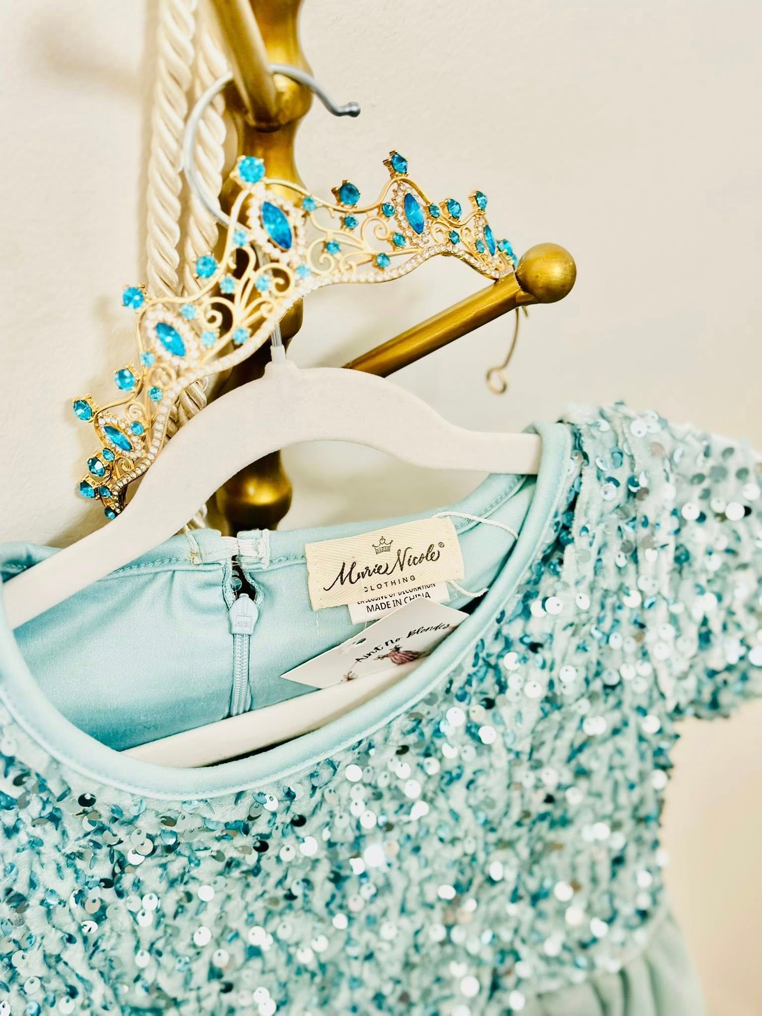 A blue sequined dress is hanging on a hanger next to a tiara.