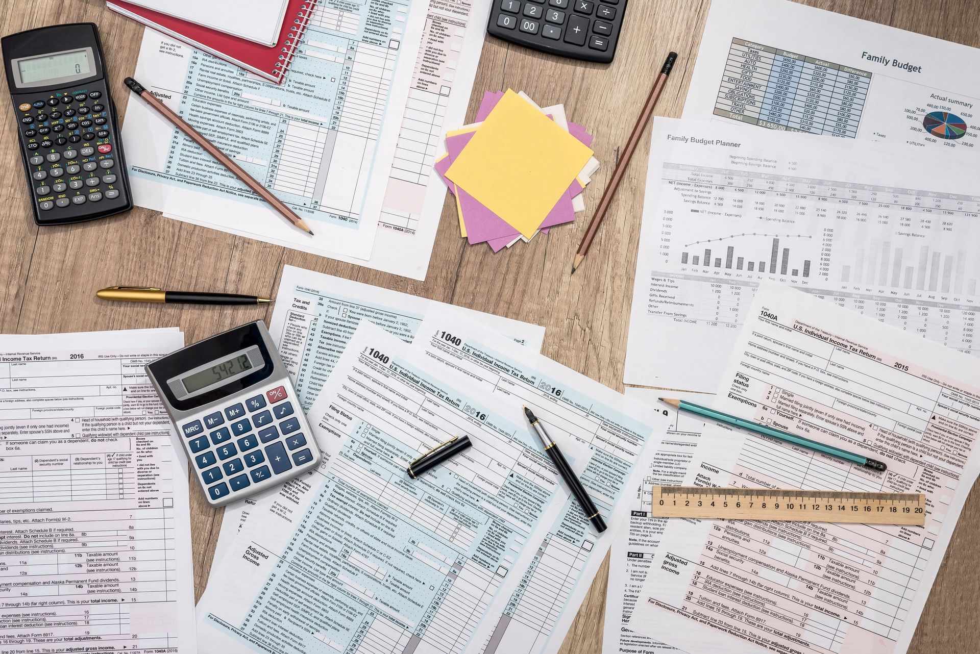 Overhead view of scattered tax forms, calculators, pens, sticky notes, and rulers on a desk