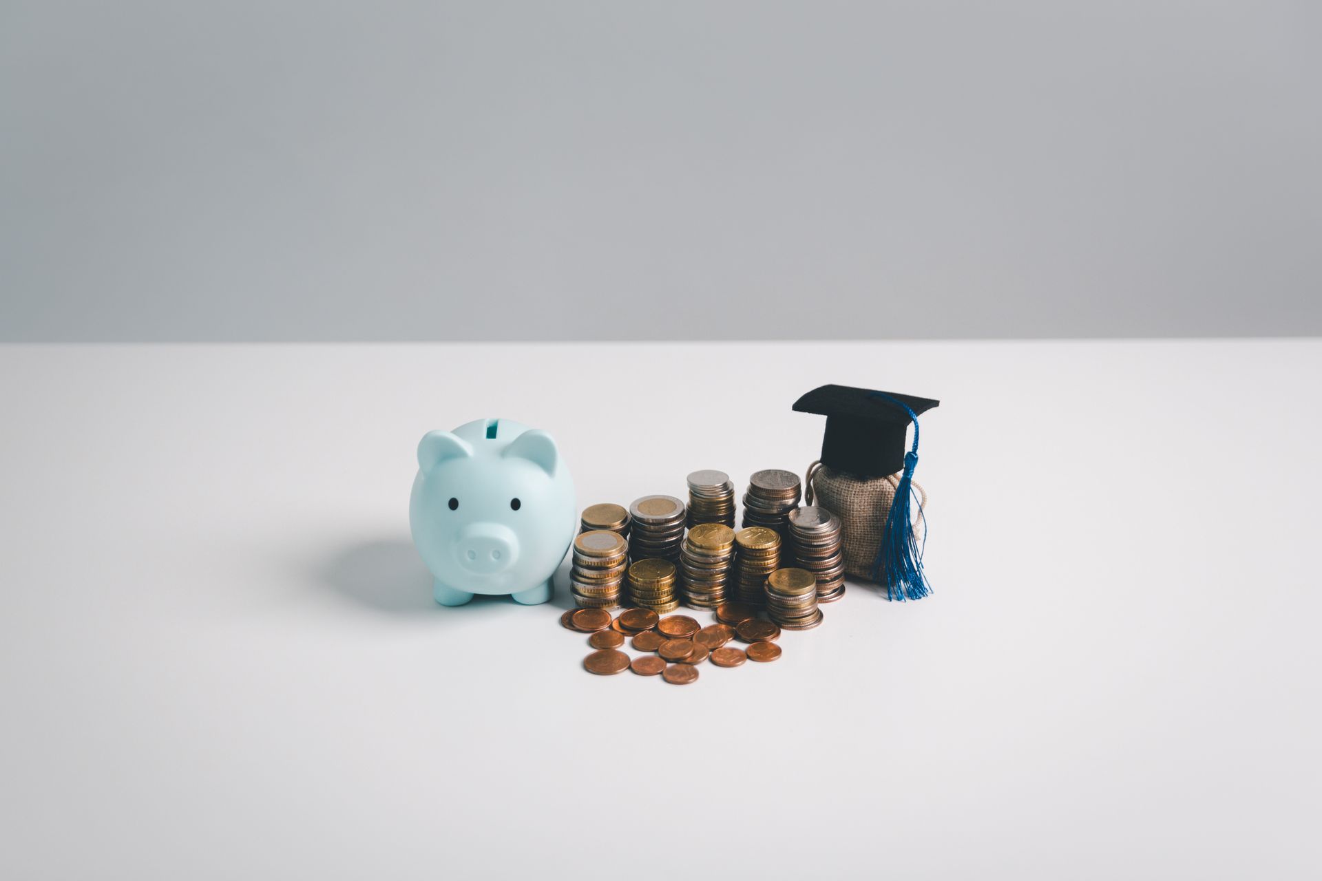 A piggy bank , stacks of coins and a graduation cap on a table.