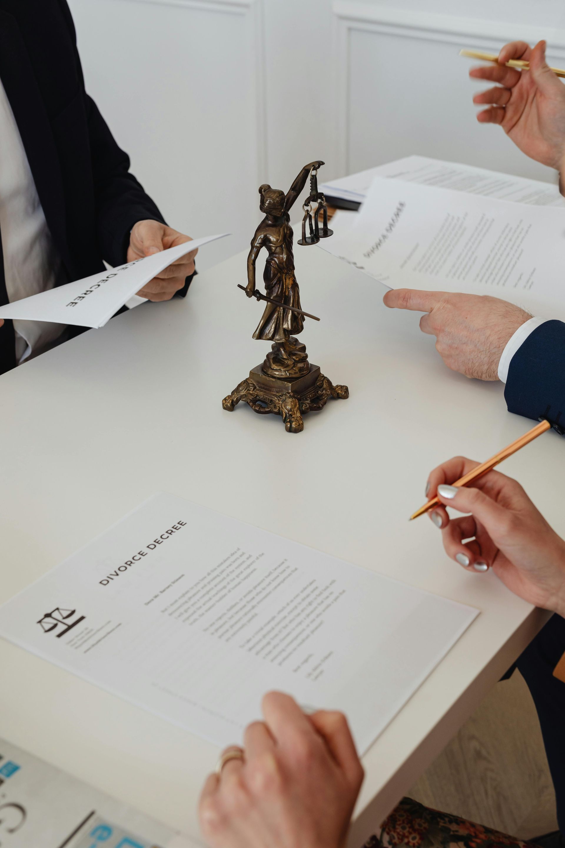 A group of people are sitting at a table with papers and a statue of justice.