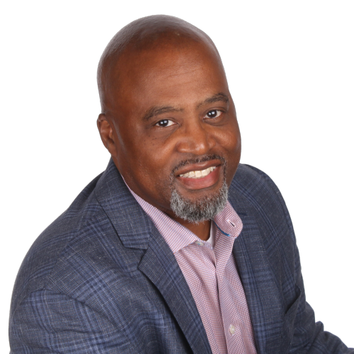 A smiling Black man with a graying beard, wearing a plaid blazer and pink shirt, against a white background.