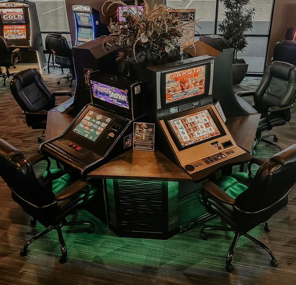 Round casino gaming table with multiple slot-style screens and black chairs around it in a dimly lit room