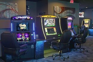Row of three gaming machines with black leather chairs in a dimly lit, modern room with patterned carpet and wall art.