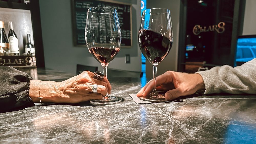Two people are sitting at a bar holding hands and drinking wine.