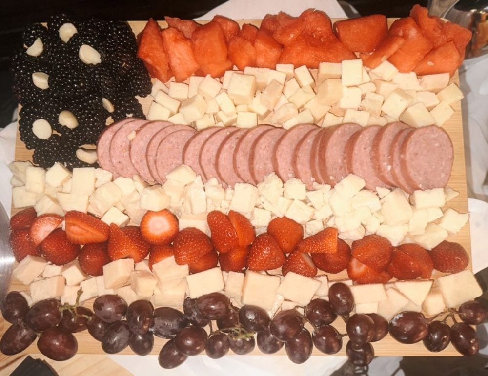 A tray of food including grapes strawberries cheese and salami in the shape of an american flag