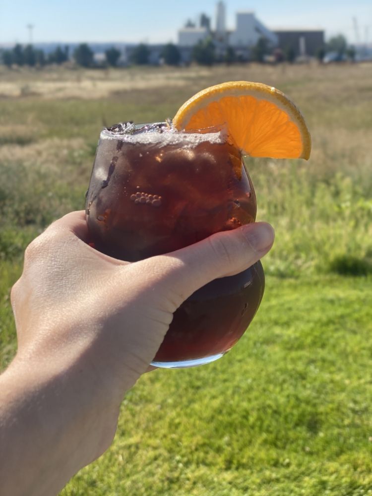 A person is holding a glass of iced tea with an orange slice on top.