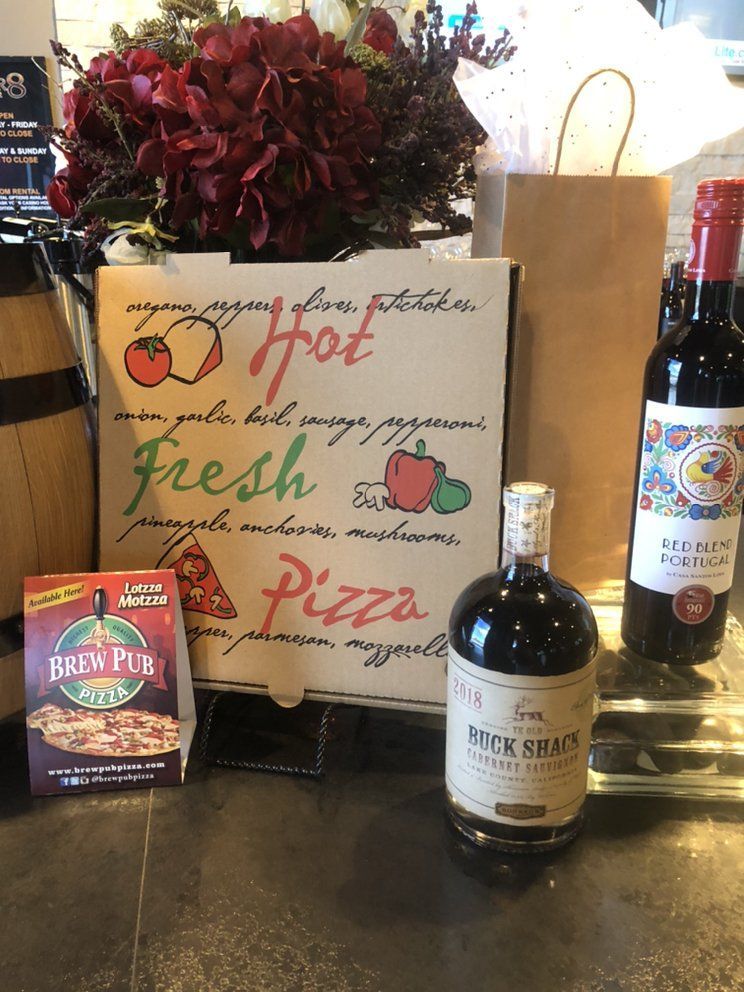 A bottle of beer , a box of pizza , and a bag of flowers are on a table.