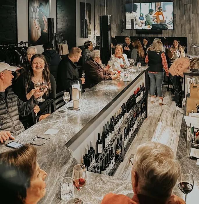 People chatting at a busy wine bar with rows of bottles on the counter