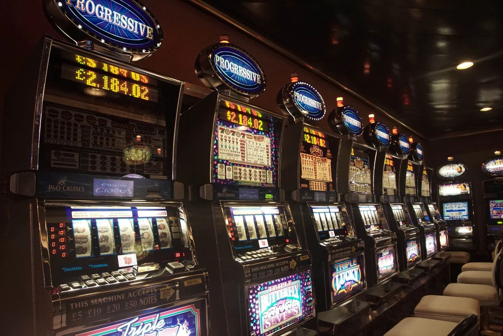 Slot machines in a casino, lit with flashing lights and displays, rows of empty seats.