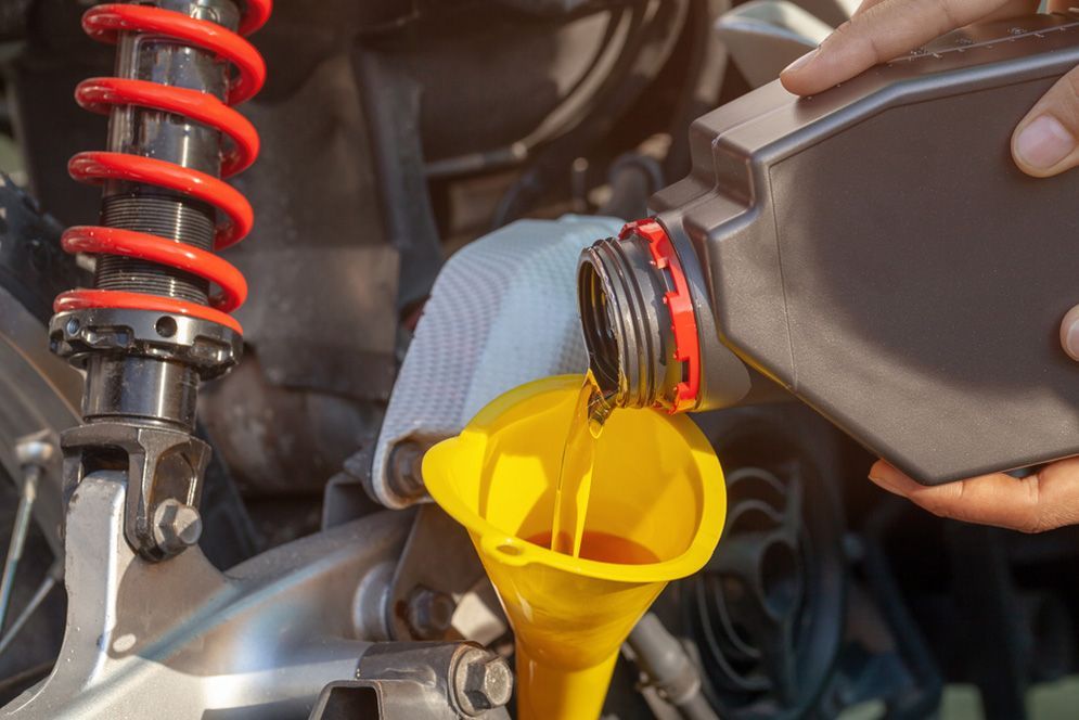 A Person is Pouring Oil Into a Yellow Funnel on a Motorcycle — Fischer Automotive in Svensson Heights, QLD