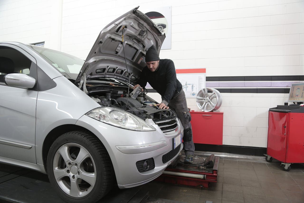 A man is working on a car with the hood up in a garage.