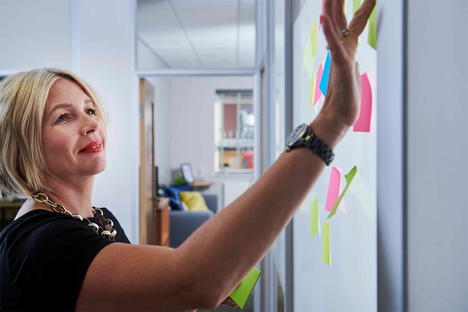 A woman is pointing at sticky notes on a whiteboard.