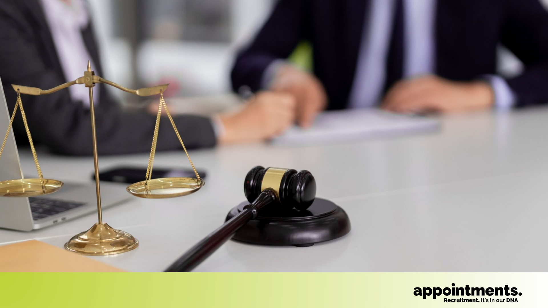 Close-up of a judge’s gavel and scales of justice on a desk with two workers reviewing documents