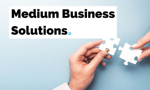 Two people are holding puzzle pieces in their hands in front of a sign that says medium business solutions.